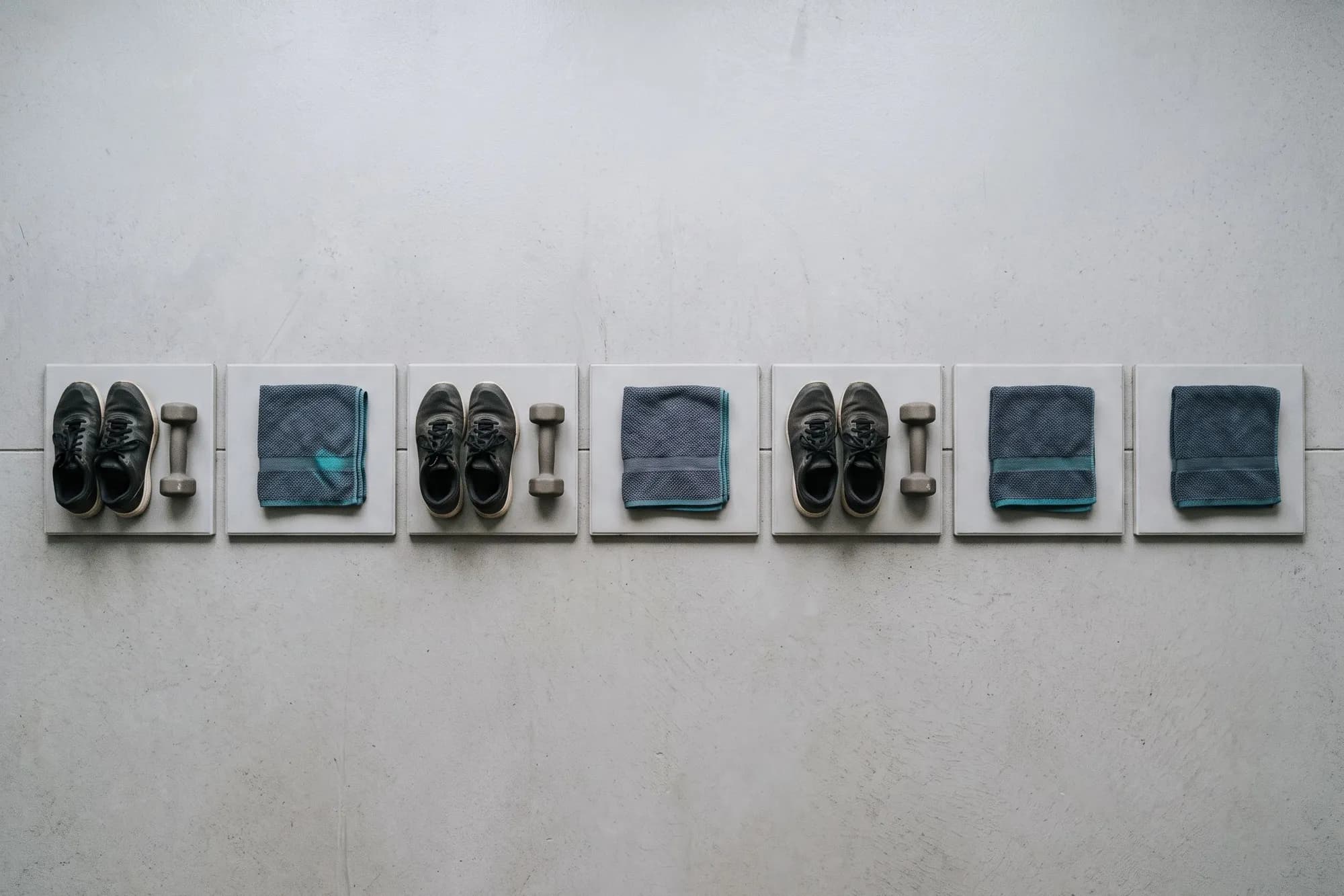Seven squares in a row like the days of a week: shoes and a dumbbell on three of them, a folded towel on the other four